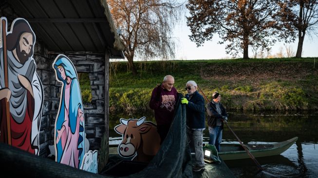 Warga saat akan memasang Instalasi Natal yang berkisah tentang kelahiran Yesus di sungai Po, Villafranca Piemonte, Turin, Italia, Selasa (6/12/2022). [MARCO BERTORELLO / AFP]
