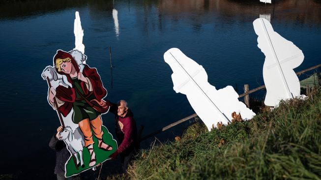 Warga saat akan memasang Instalasi Natal yang berkisah tentang kelahiran Yesus di sungai Po, Villafranca Piemonte, Turin, Italia, Selasa (6/12/2022). [MARCO BERTORELLO / AFP]
