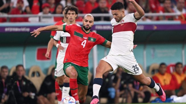 Gelandang Maroko Sofyan Amrabat berebut bola dengan pemain Portugal di perempat final Piala Dunia 2022 yang digelar di Al Thumama Stadium, Sabtu (10/12/2022). [AFP]