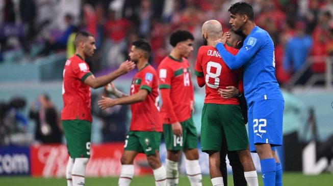 Kiper timnas Maroko #22 Ahmed Reda Tagnaouti menghibur gelandang Maroko #08 Azzedine Ounahi pada akhir pertandingan semifinal Piala Dunia Qatar 2022 antara Prancis vs Maroko di Stadion Al-Bayt di Al Khor, utara Doha pada Kamis (15/12/2022) dini hari WIB. Maroko kalah 0-2 dari Prancis.Kirill KUDRYAVTSEV / AFP