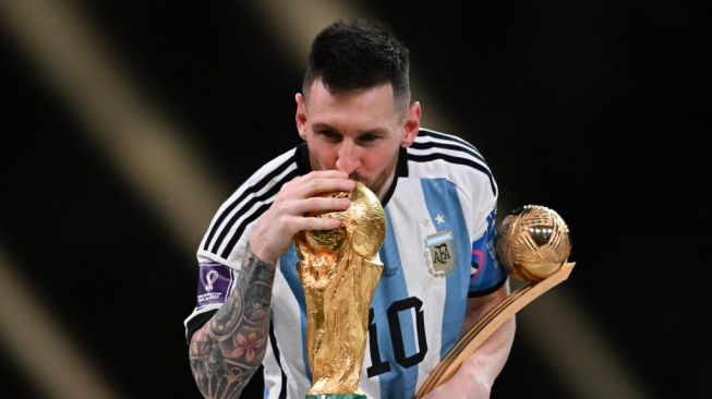 Penyerang Timnas Argentina, Lionel Messi sambil memegang trofi bola emas sebagai pemain terbaik Piala Dunia 2022, mencium trofi Piala Dunia di Stadion Lusail, Qatar, Senin (19/12/2022) dini hari WIB. [Kirill KUDRYAVTSEV / AFP]