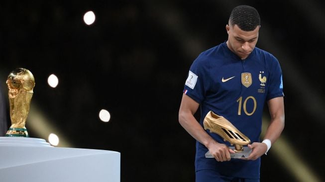 Penyerang Prancis Kylian Mbappe berjalan melewati trofi Piala Dunia saat ia memegang penghargaan Sepatu Emas selama upacara trofi Piala Dunia 2022 Qatar setelah pertandingan final sepak bola antara Argentina dan Prancis di Stadion Lusail di Lusail, utara Doha, Qatar, Minggu (18/12/2022). [FRANCK FIFE / AFP]