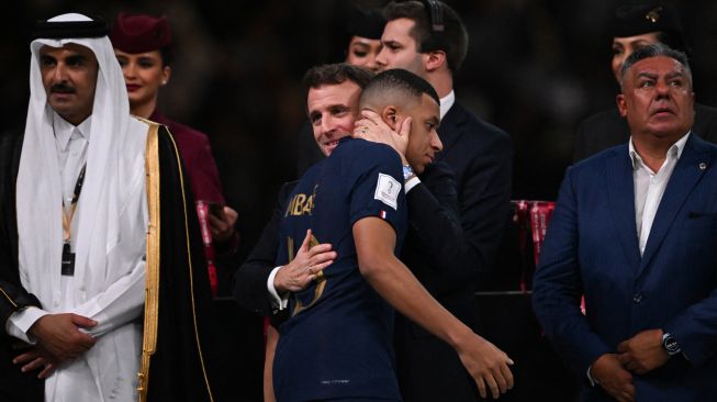 Presiden Prancis Emmanuel Macron menghibur penyerang Prancis Kylian Mbappe selama upacara trofi setelah Prancis kalah dalam pertandingan sepak bola final Piala Dunia 2022 antara Argentina dan Prancis di Stadion Lusail di Lusail, utara Doha, Qatar, Minggu (18/12/2022). [Kirill KUDRYAVTSEV / AFP]