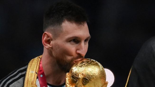 Penyerang Timnas Argentina, Lionel Messi mencium trofi Piala Dunia usai juara di Qatar 2022. [FRANCK FIFE / AFP]