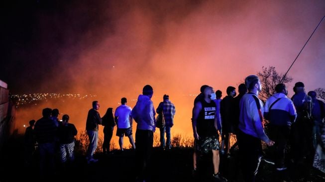 Orang-orang menyaksikan kebakaran hutan melanda perbukitan Vina del Mar, tempat ratusan rumah berada, di Wilayah Valparaiso, Chili, Jumat (23/12/2022). [JAVIER TORRES/AFP]