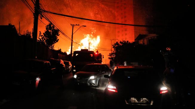 Kendaraan bergerak di sepanjang jalan saat kebakaran hutan melanda perbukitan Vina del Mar, tempat ratusan rumah berada, di Wilayah Valparaiso, Chili, Jumat (23/12/2022). [JAVIER TORRES/AFP]