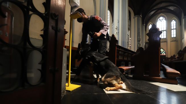 Personel kepolisian membawa anjing pelacak saat melakukan sterilisasi dan pengamanan di Gereja Katedral, Jakarta Pusat, Sabtu (24/12/2022). [Suara.com/Alfian Winanto]