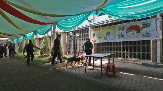 Personel kepolisian membawa anjing pelacak saat melakukan sterilisasi dan pengamanan di Gereja Katedral, Jakarta Pusat, Sabtu (24/12/2022). [Suara.com/Alfian Winanto]