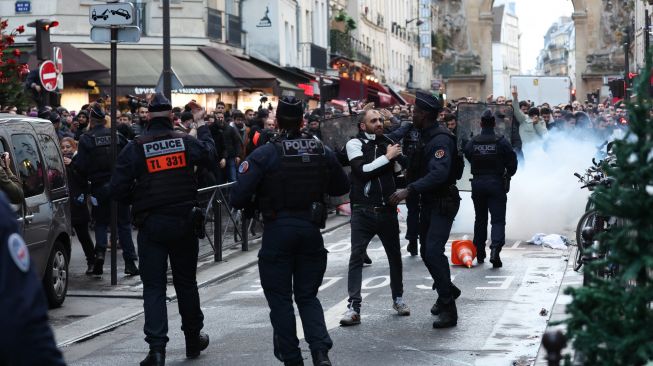 Para pengunjuk rasa bentrok dengan petugas polisi anti huru hara Prancis menyusul insiden penembakan kepada komunitas Suku Kurdi di Paris, Prancis, Jumat (23/12/2022). [Thomas SAMSON / AFP]