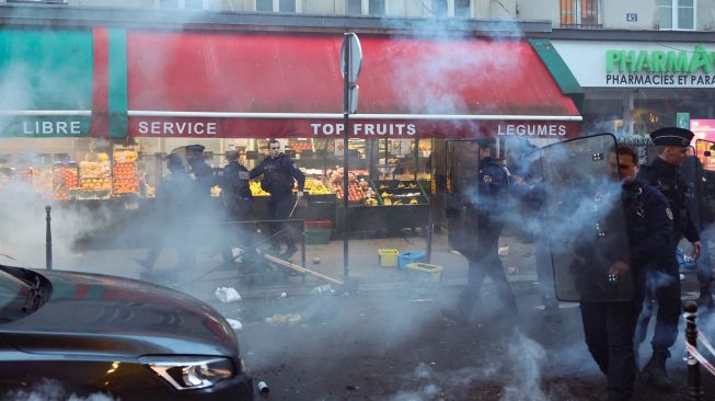 Petugas polisi anti huru hara Prancis berlari untuk membubarkan pengunjuk rasa selama bentrokan menyusul menyusul insiden penembakan kepada komunitas Suku Kurdi di Paris, Prancis, Jumat (23/12/2022). [Thomas SAMSON / AFP]