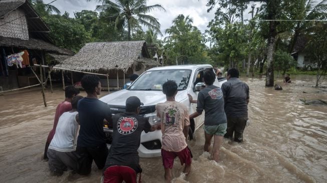 Warga mendorong mobil yang mogok saat banjir menggenangi kawasan Patia, Pandeglang, Banten, Selasa (27/12/2022). [ANTARA FOTO/Muhammad Bagus Khoirunas].