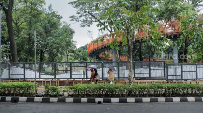 Pejalan kaki melintas di depan proyek pemasangan pagar di Tebet Eco Park, Tebet, Jakarta Selatan, Jumat (30/12/2022). [Suara.com/Alfian Winanto]