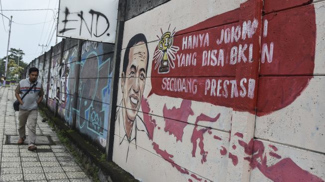 Warga melintas di dekat mural yang bertuliskan “Hanya Jokowi yang bisa bikin segudang prestasi” di Kabupaten Ciamis, Jawa Barat, Jumat (30/12/2022). [ANTARA FOTO/Adeng Bustomi].