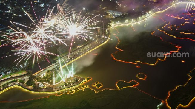 Warga menyaksikan pesta kembang api saat perayaan malam Tahun Baru 2023 di Danau Archipelago, Taman Mini Indonesia Indah (TMII), Jakarta Timur, Minggu (1/1/2023). [Suara.com/Alfian Winanto]