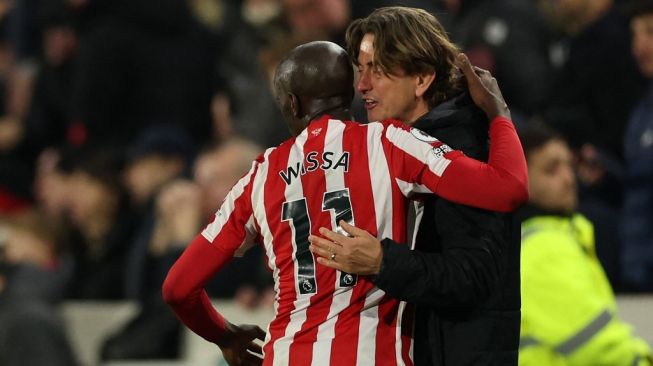 Pelatih Brentford, Thomas Frank (kanan) berpelukan dengan penyerang Yoane Wissa setelah mencetak gol ke gawang Liverpool pada laga Liga Inggris di Stadion Gtech Community, London, Selasa (3/1/2023) dini hari WIB. [Adrian DENNIS / AFP]