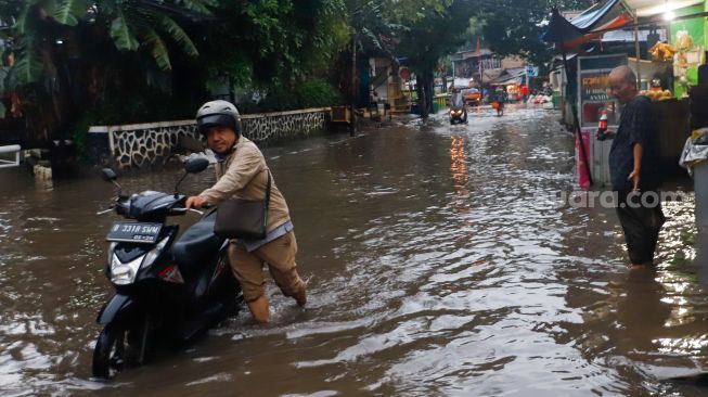 Warga mendorong kendaraannya melewati banjir di Jalan Kemang Utara IX, Jakarta Selatan, Rabu (4/1/2023). [Suara.com/Alfian Wina Winanto]