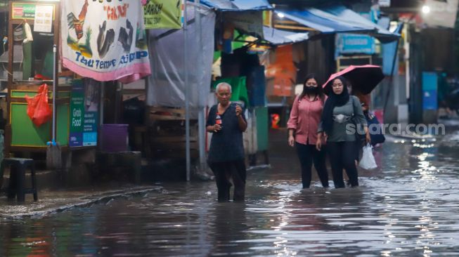 Warga berjalan melewati banjir di Jalan Kemang Utara IX, Jakarta Selatan, Rabu (4/1/2023). [Suara.com/Alfian Wina Winanto]