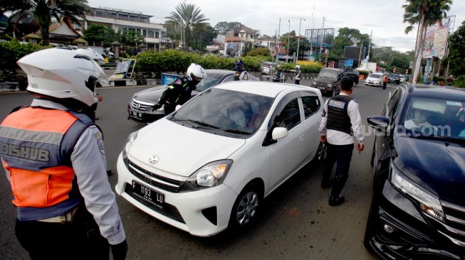 Petugas Sat Lantas Polres Bogor dan petugas Dishub Kabupaten Bogor mengarahkan kendaraan wisatawan saat penyekatan kendaraan nomor polisi ganjil genap di jalur wisata Puncak, Gadog, Kabupaten Bogor, Jawa Barat, Minggu (22/1/2023). [ANTARA FOTO/Yulius Satria Wijaya/aww]