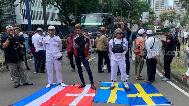 Massa yang tergabung dalam PA 212 injak bendera Belanda dan Swedia saat aksi di depan Kedutaan Besar (Kedubes) Swedia, Kuningan, Jakarta Selatan pada Senin (30/1/2023). [Suara.com/Yamual]