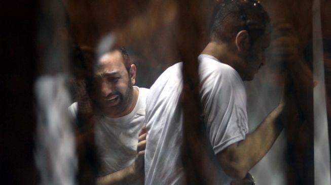 Para terdakwa bereaksi di balik jeruji besi setelah vonis dalam sidang ulang mereka atas kerusuhan stadion tahun 2012 di kota kanal Port Said yang menewaskan 74 orang, pada 9 Juni 2015 di sebuah pengadilan di ibu kota Mesir, Kairo. Pengadilan menjatuhkan hukuman mati terhadap 11 penggemar sepak bola atas kerusuhan yang pecah ketika pendukung tim tuan rumah Al-Masry dan Al-Ahly bentrok setelah pertandingan liga utama antara kedua klub. FOTO AFP / AHMED GAMIL.