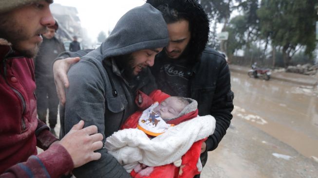 Seorang pria Suriah menangis saat menggendong jenazah putranya yang tewas dalam gempa bumi di kota Jandaris, provinsi Aleppo, Suriah, Senin (6/2/2023). [Bakr ALKASEM / AFP]
