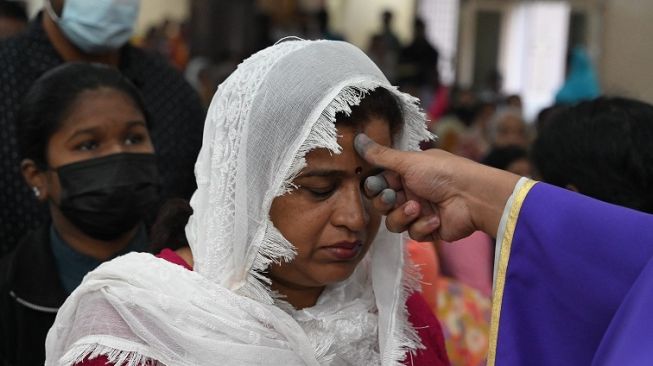 Pastor Prince Xavier, seorang Imam Katolik tengah menorehkan simbol salib dengan abu di dahi seorang umat dalam Misa Rabu Abu di Saint Anthony's Shrine Secunderabad, twin sister dari Hyderabad, India pada 22 Februari 2023 [AFP/Noah Selam].