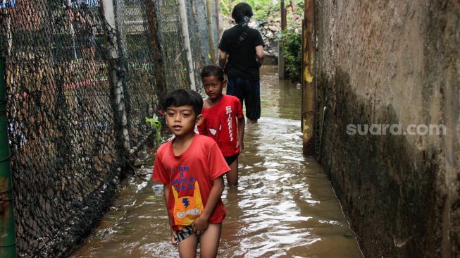 Anak-anak berjalan melewati banjir di kawasan pemukiman penduduk, Rawajati, Jakarta Selatan, Senin (27/2/2023). [Suara.com/Alfian Winanto]