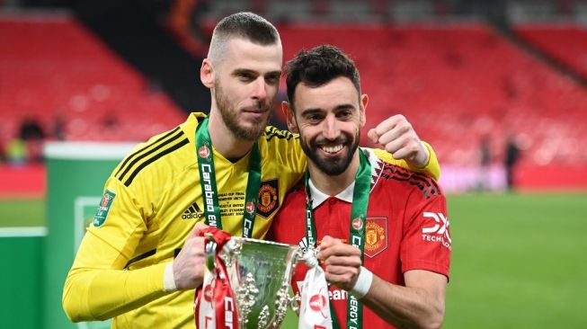 Kiper Manchester United asal Spanyol, David de Gea dan Bruno Ferandes (kanan) melakukan selebrasi dengan mengangkat trofi usai membantu timnya menjuarai Piala Liga Inggris 2023 dengan mengalahkan Newcastle United 2-0 pada laga final di Stadion Wembley, London, Minggu (26/2/2023) malam WIB. [AFP]