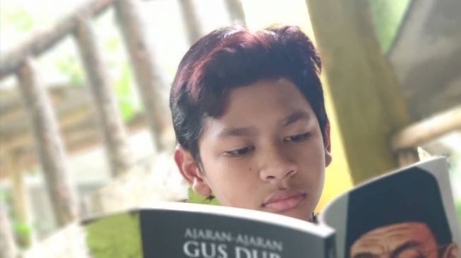 Putri sulung mendingan Gus Dur dan Sinta Nuriyah, Alissa Wahid mengunggah foto David kecil tengah membaca buku Gus Dur. (Twitter @/AlissaWahid)