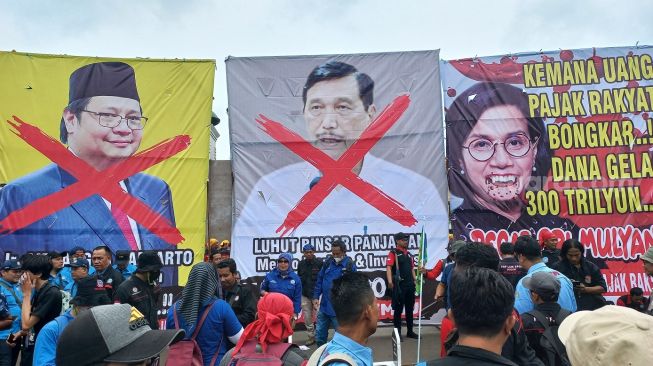 Massa tolak Perppu Cipta Kerja membawa baliho besar bergambar wajah 3 menteri di pemerintahan Joko Widodo, pada Selasa (14/3/2023). (Suara.com/Faqih)