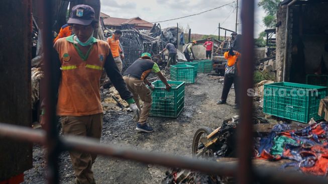 Petugas membersihkan sisa-sisa kebakaran di tempat penampungan hewan di Duren Sawit, Jakarta Timur, Senin (27/3/2023). [Suara.com/Alfian Winanto]