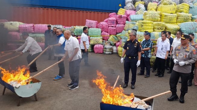 Pemusnahan pakaian bekas impor dengan cara dibakar di tempat penimbunan pebaean (TPP) Bea Cukai, Cikarang Utara, Kabupaten Bekasi, Jawa Barat, Selasa (28/3). (Suara.com / Danan arya)