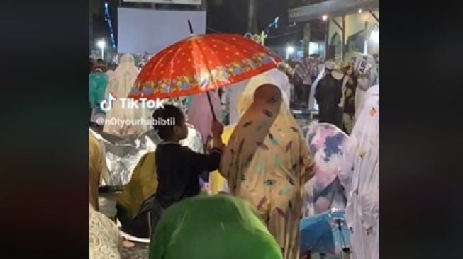 Bikin Haru, Momen Anak Laki-laki Payungi Ibu Salat Tarawih saat Hujan Deras