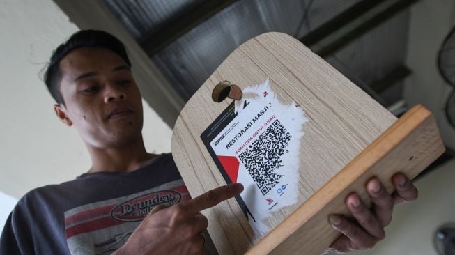 Seorang jemaah menunjukkan sisa stiker kode QRIS palsu pada kotak amal yang dipasang oleh oknum warga di Masjid Nurul Iman Blok M Square, Jakarta, Selasa (11/4/2023). [ANTARA FOTO/Aditya Pradana Putra].