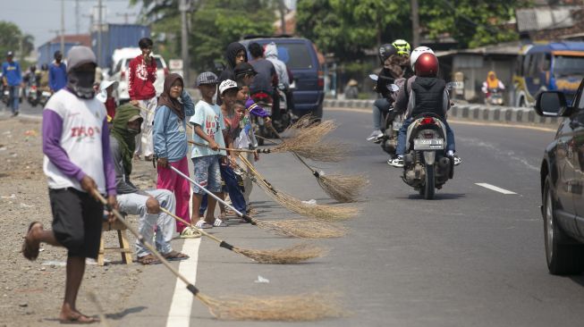 Sejumlah warga menunggu pengendara memberi sedekah dengan melempar uang di Jembatan Sewo, Jalur Pantura Sukra Indramayu, Jawa Barat, Senin (17/4/2023).[ANTARA FOTO/Dedhez Anggara].