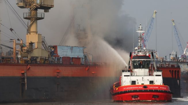 Petugas dengan menggunakan kapal tunda (tug boat) menyemprotkan air ke KM Anugerah Mandiri 8 yang terbakar di atas dok apung PT DOK dan Perkapalan Surabaya, Pelabuhan Tanjung Perak, Surabaya, Jawa Timur, Rabu (19/4/2023). [ANTARA FOTO/Didik Suhartono]