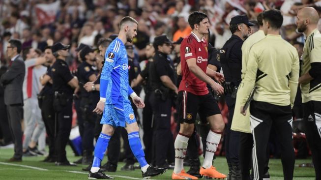 Kiper Manchester United, David de Gea (jersey biru) dan bek Harry Maguire (merah) meninggalkan lapangan usai laga perempat final Liga Europa kontra Sevilla di Stadion Ramon Sanchez Pizjuan, Sevilla, Spanyol, Jumat (21/4/2023) dini hari WIB. [CRISTINA QUICLER / AFP]