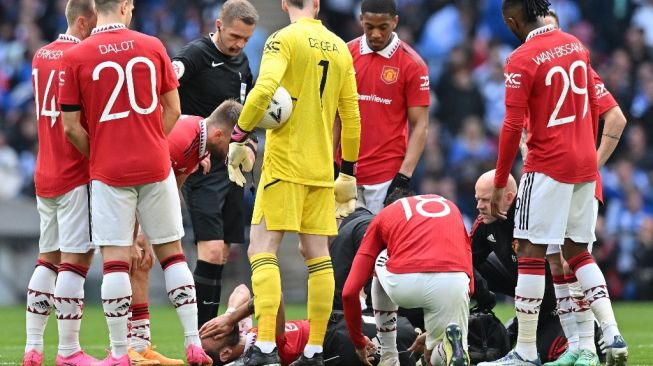 Gelandang Manchester United, Bruno Fernandes (bawah) mendapatkan perawatan usai mengalami cedera di laga semifinal Piala FA kontra Brighton di Stadion Wembley, London, Inggris, Minggu (23/4/2023) malam WIB. [G. KIRK / AFP]