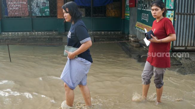 Warga melintasi banjir yang menggenangi Pondok Gede Permai, Bekasi, Jawa Barat, Kamis (4/5/2023). [Suara.com/Alfian Winanto]