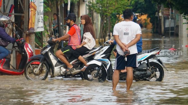 Warga melintasi banjir yang menggenangi Pondok Gede Permai, Bekasi, Jawa Barat, Kamis (4/5/2023). [Suara.com/Alfian Winanto]