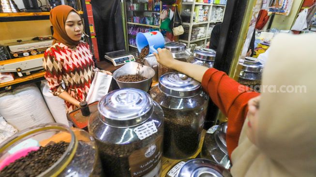 Pedagang memasukkan kopi ke dalam kemasan untuk pembeli di Dunia Kopi, Pasar Santa, Jakarta Selatan, Jumat (5/5/2023). [Suara.com/Alfian Winanto]