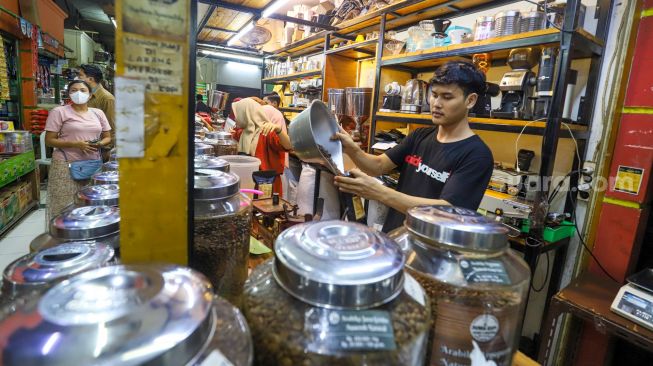 Pedagang memasukkan kopi ke dalam kemasan untuk pembeli di Dunia Kopi, Pasar Santa, Jakarta Selatan, Jumat (5/5/2023). [Suara.com/Alfian Winanto]
