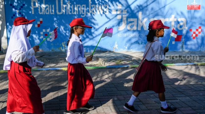 Sejumlah pelajar berjalan dengan membawa bendera Merah Putih saat peresmian Kampung Bahari Nusantara (KBN) di Pulau Untung Jawa, Kepulauan Seribu, Jakarta, Senin (15/5/2023). [ANTARA FOTO/M Risyal Hidayat/tom]