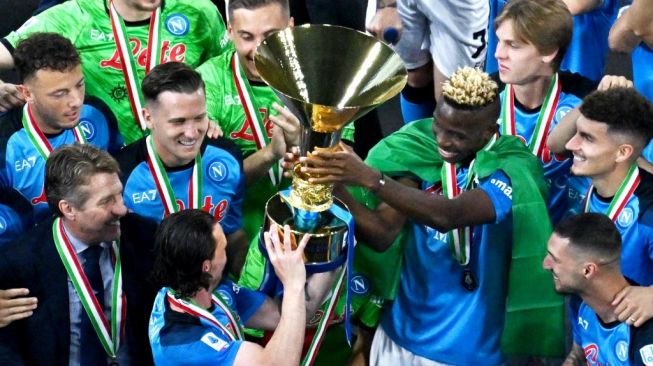 Penyerang Napoli dengan syarat Nigeria Victor Osimhen memegang trofi Liga Italia saat ia serta rekan satu timnya merayakan Scudetto musim ini usai laga pekan ke-38 atau terakhir Serie A 2022-2023 kontra Sampdoria pada 4 Juni 2023 di dalam stadion Diego-Maradona di area Naples.Tiziana FABI/AFP.