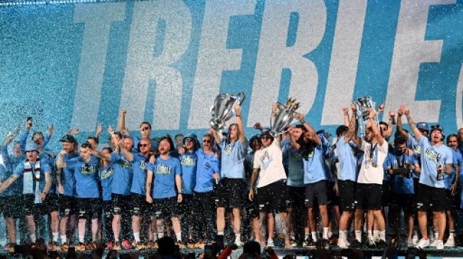 Para pemain Manchester City merayakan di atas panggung dengan trofi mereka setelah parade kemenangan bus atap terbuka untuk kemenangan mereka di Piala Eropa, Piala FA, dan Liga Premier, di Manchester, Inggris utara pada 12 Juni 2023. Oli SCARFF/AFP
