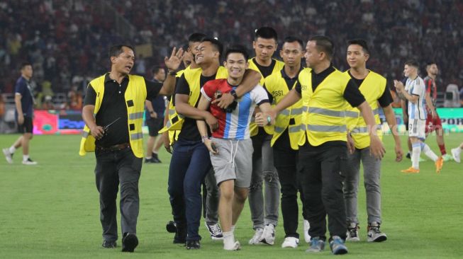 Seorang suporter mengenakan jersey Timnas Indonesia dan Argentina diamankan usai masuk ke dalam lapangan Stadion Utama Gelora Bung Karno (SUGBK), Senayan, Jakarta, Senin (19/6/2023). [Suara.com/Dwi Bowo Raharjo]