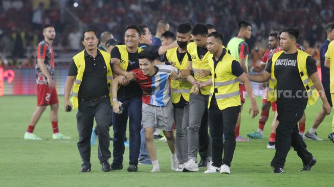 Seorang suporter mengenakan jersey Timnas Indonesia dan Argentina diamankan usai masuk ke dalam lapangan Stadion Utama Gelora Bung Karno (SUGBK), Senayan, Jakarta, Senin (19/6/2023). [Suara.com/Dwi Bowo Raharjo]