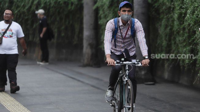 Pesepeda memakai masker saat melintas di Kawasan Bundaran HI, Jakarta, Rabu (21/6/2023). [Suara.com/Alfian Winanto]