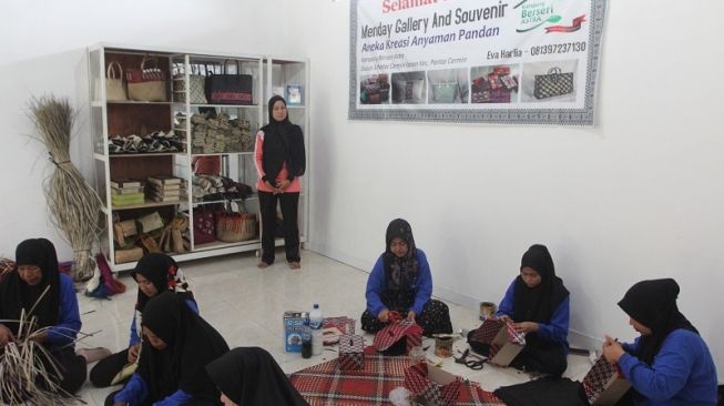 Tokoh penggerak KBA Desa Pantai Cermin Kanan dan pencetus Kelompok Perempuan Kanan Kreatif (KPKK) Eva Harlia (tengah) bersama anggota KPKK saat membuat anyaman di rumah kreasi anyaman pandan Menday Gallery and Souvenir [Astra]