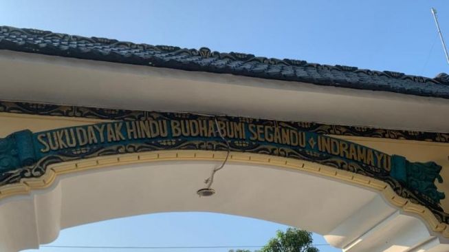 Gapura bertuliskan Suku Dayak Hindu Budha Bumi Segandhu Indramayu menjadi penanda tempat komunitas Suku Dayak Indramayu tinggal. [Suara.com/Rakha Arlyanto]
